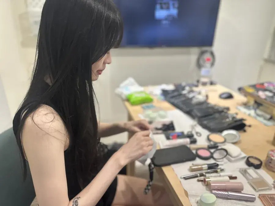 化妝師坐在桌前挑選化妝品，桌上擺滿彩妝與刷具