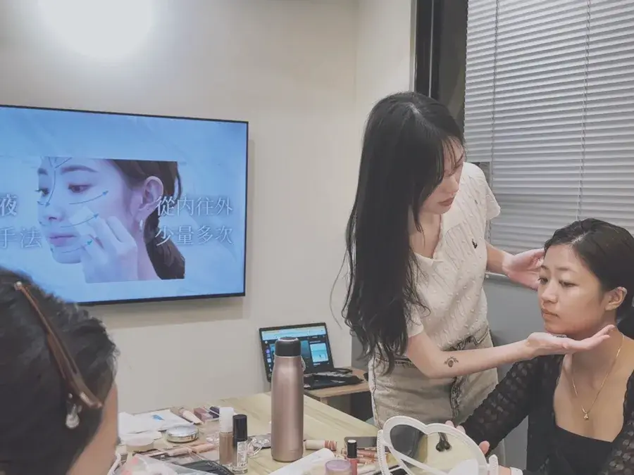 彩妝課教室一景：化妝師為學員上妝，牆上螢幕播放臉部示意圖
